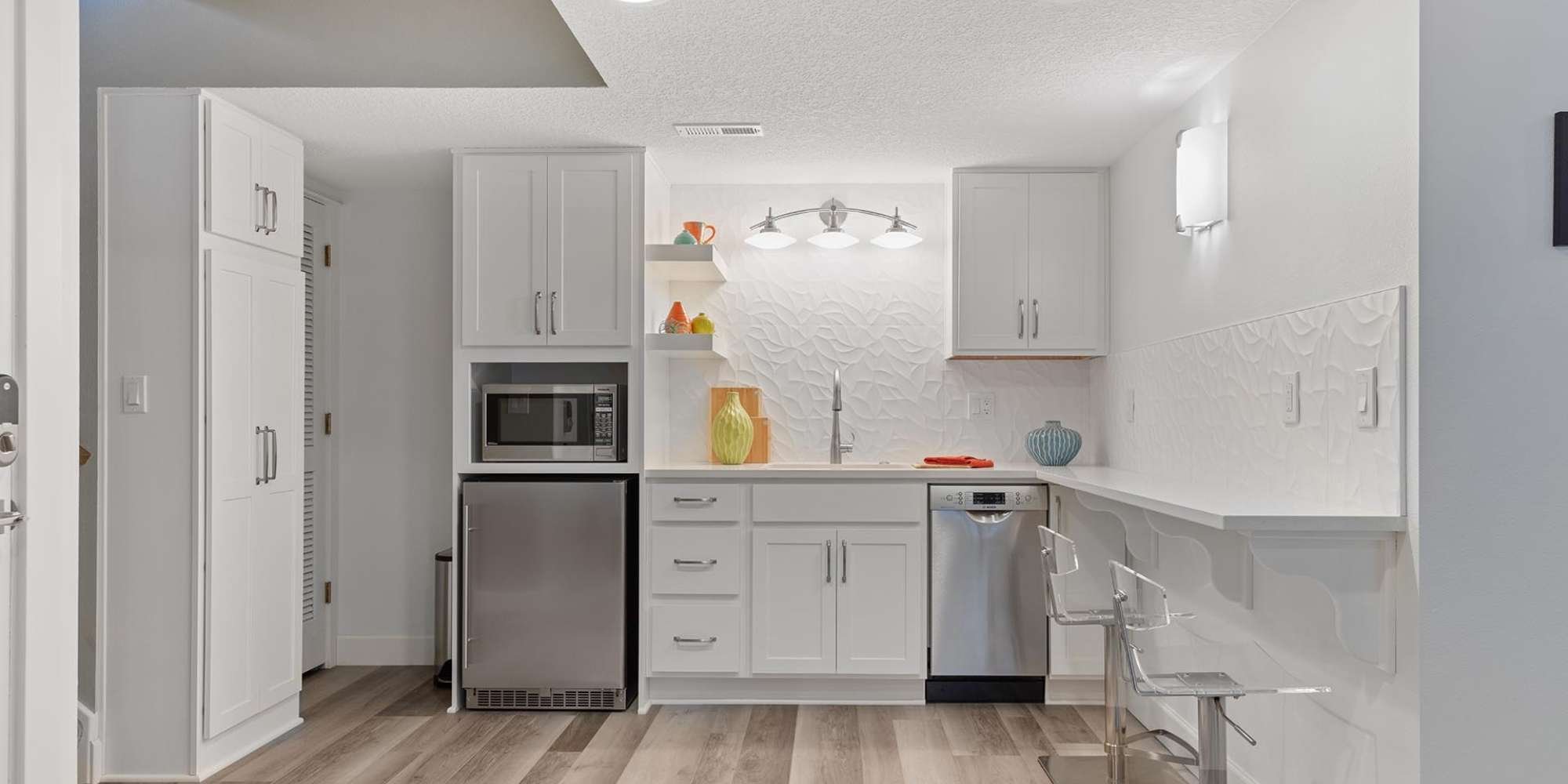 Modern basement kitchen remodel in Portland, OR featuring white cabinetry, bar seating, and built-in appliances