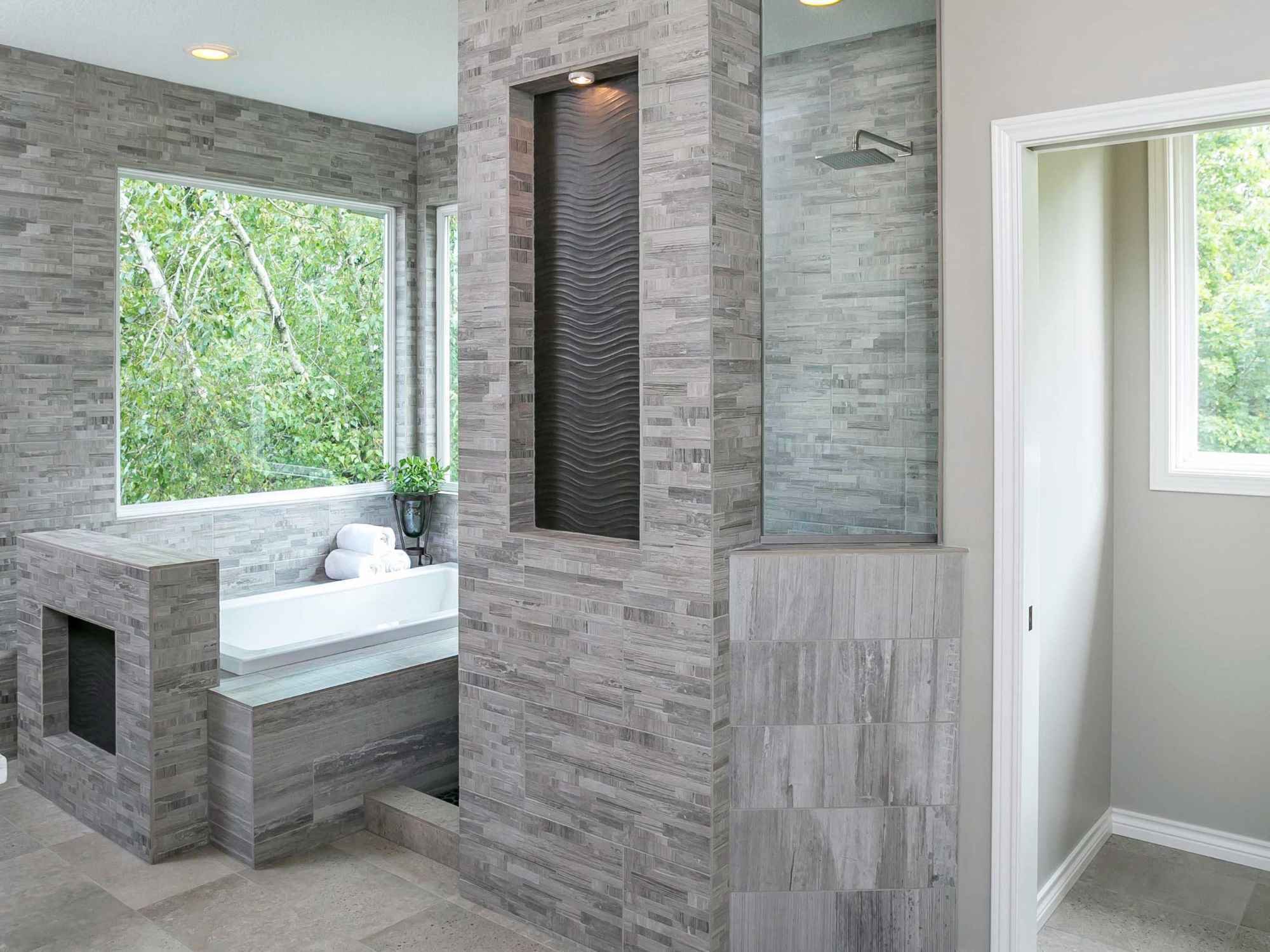 Primary bathroom remodel with a grey tile walk-in shower and a soaking tub beneath a large window by Creekstone Design + Remodel in Portland, OR Primary bathroom remodel with a grey tile walk-in shower and a soaking tub beneath a large window by Creekstone Design + Remodel in Portland, OR
