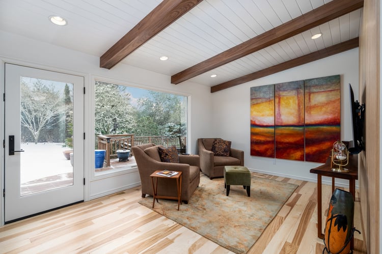 Renovated den featuring warm wood accents, modern seating, and a large abstract painting, designed for a whole home remodel in Portland, OR by Creekstone Design + Remodel