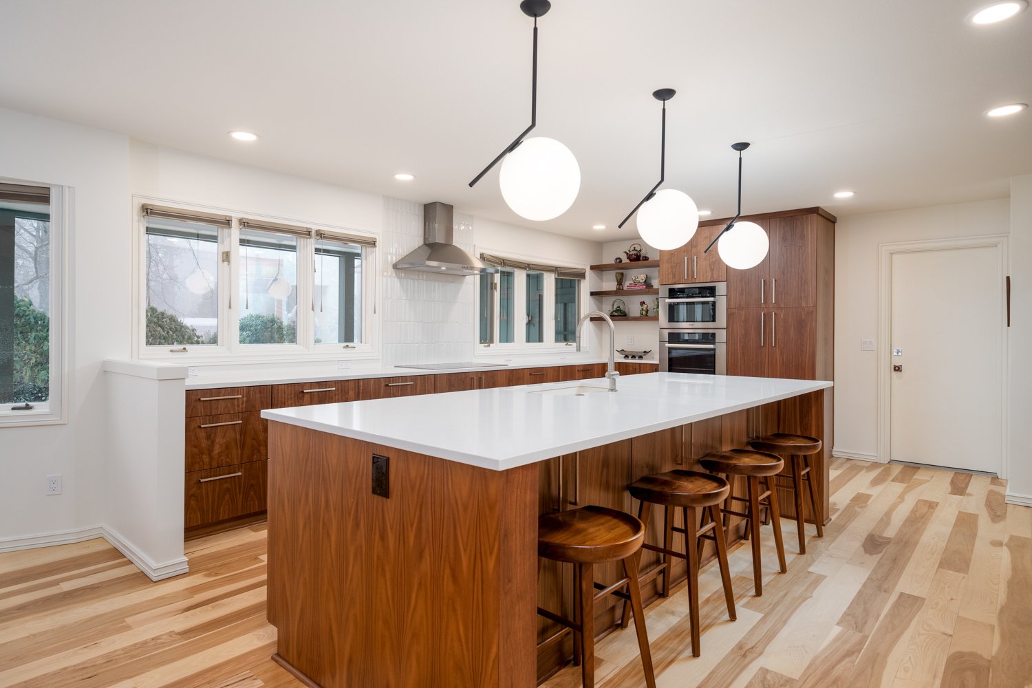 A modern kitchen with wood cabinetry, white quartz countertops, and globe pendant lights, part of a whole home remodel in Portland, OR by Creekstone Design + Remodel