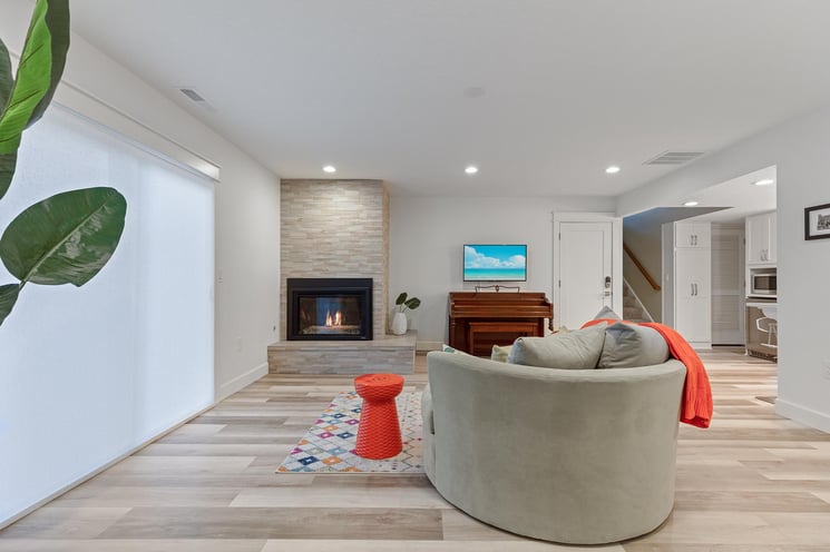 Bright entertainment space featuring stone fireplace and access to outdoor living space in basement remodel in Portland, OR by Creekstone Design + Remodel