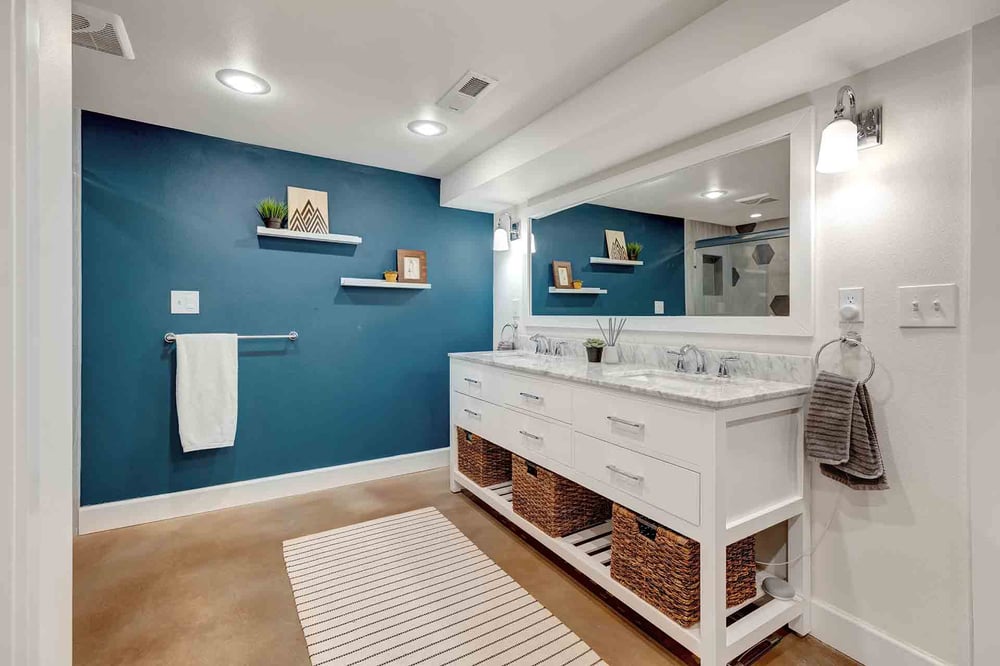 Remodeled basement bathroom with dark blue statement wall, storage drawers, and double sinks