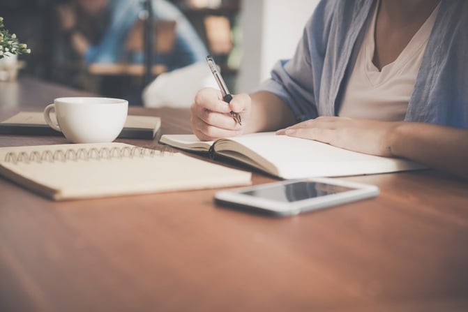 woman-writing-on-a-notebook-beside-teacup-and-tablet-733856-1