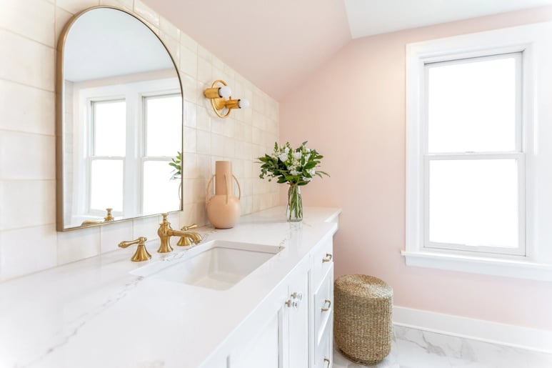 Remodeled bathroom featuring baby pink walls, white tile backsplash, and brass fixtures by Creekstone Design + Remodel
