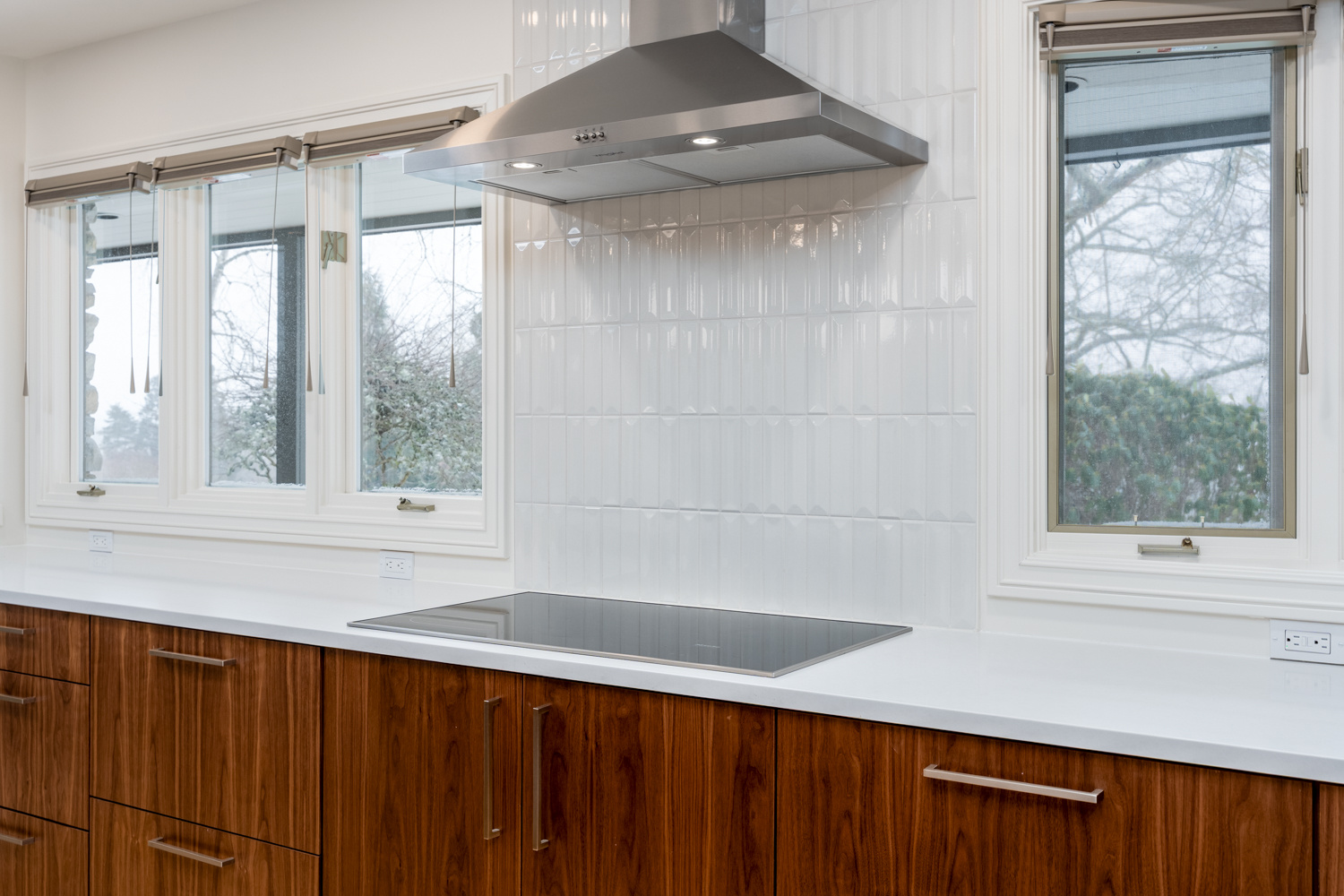 A kitchen with a clean, minimalist aesthetic featuring a built-in cooktop, modern range hood, and wood cabinets, designed for a whole home remodel in Portland, OR by Creekstone Design + Remodel