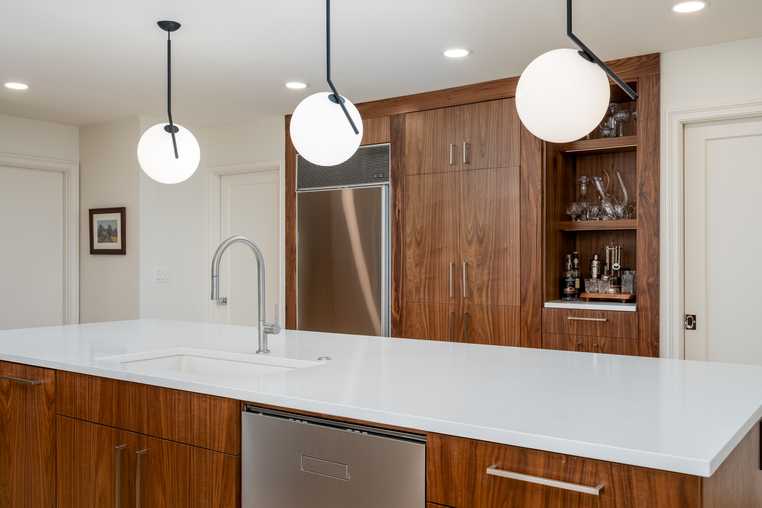 A modern kitchen with a sleek island, stainless steel dishwasher, and elegant pendant lighting, part of a whole home remodel in Portland, OR by Creekstone Design + Remodel