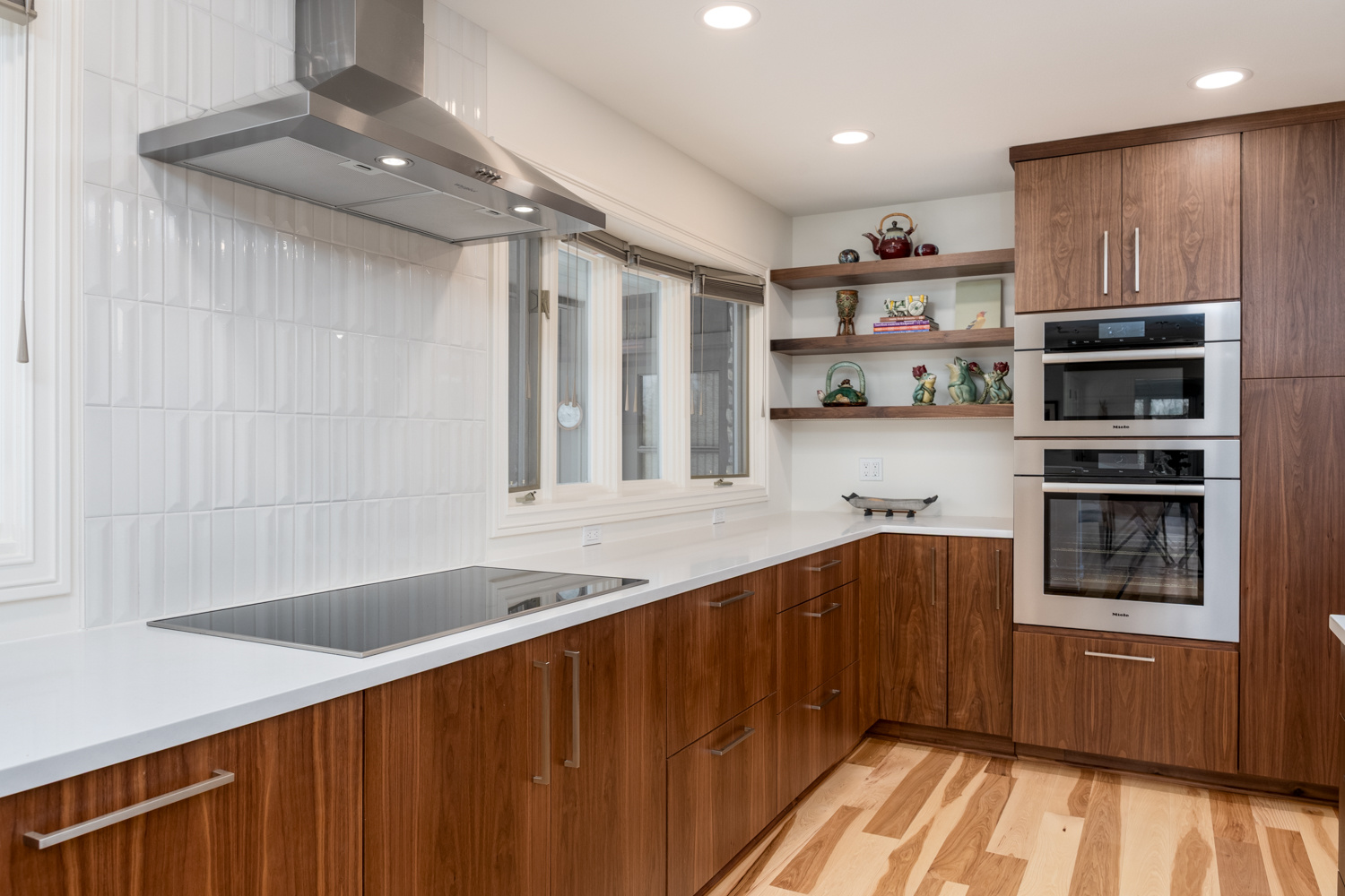 A modern kitchen with sleek wood cabinetry, white countertops, and a built-in cooktop, part of a whole home remodel in Portland, OR by Creekstone Design + Remodel