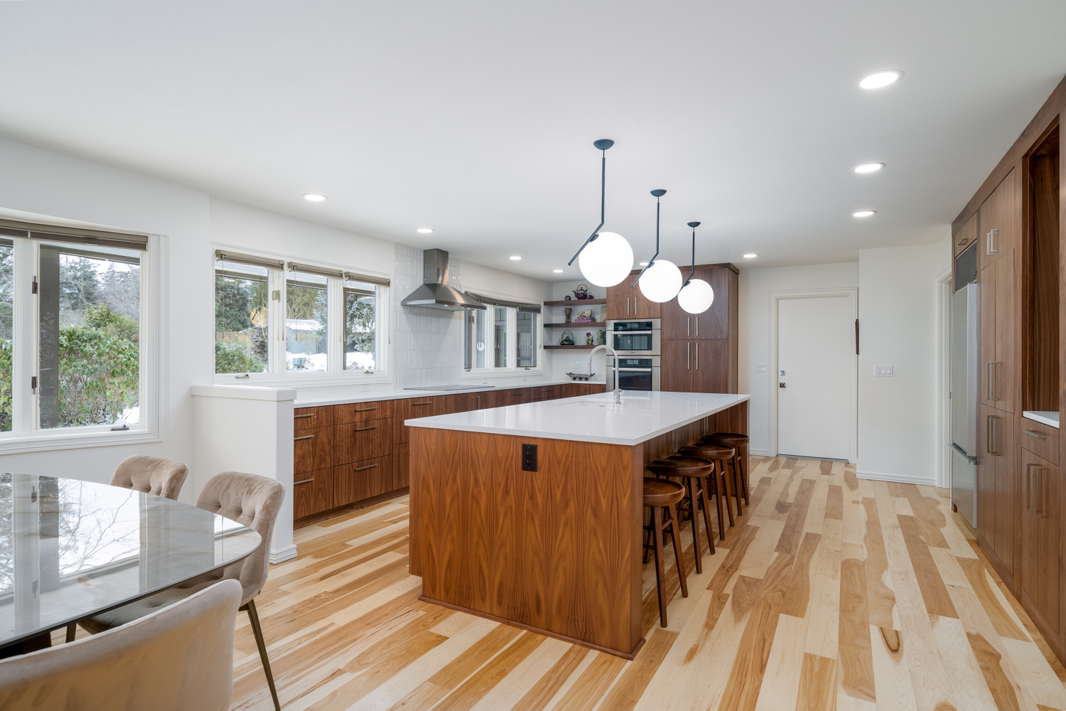 A spacious kitchen with a large island, globe pendant lights, and rich wood cabinetry, part of a whole home remodel in Portland, OR by Creekstone Design + Remodel