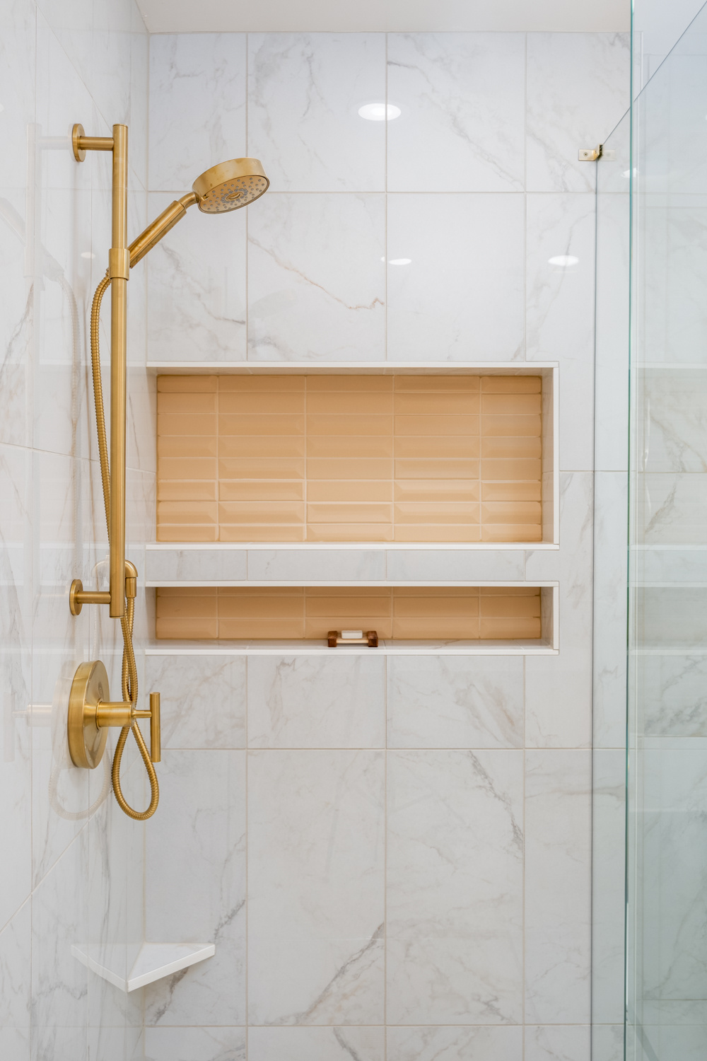 Close-up of a luxury shower with gold fixtures, built-in storage, and marble tile walls, part of a whole home remodel in Portland, OR by Creekstone Design + Remodel