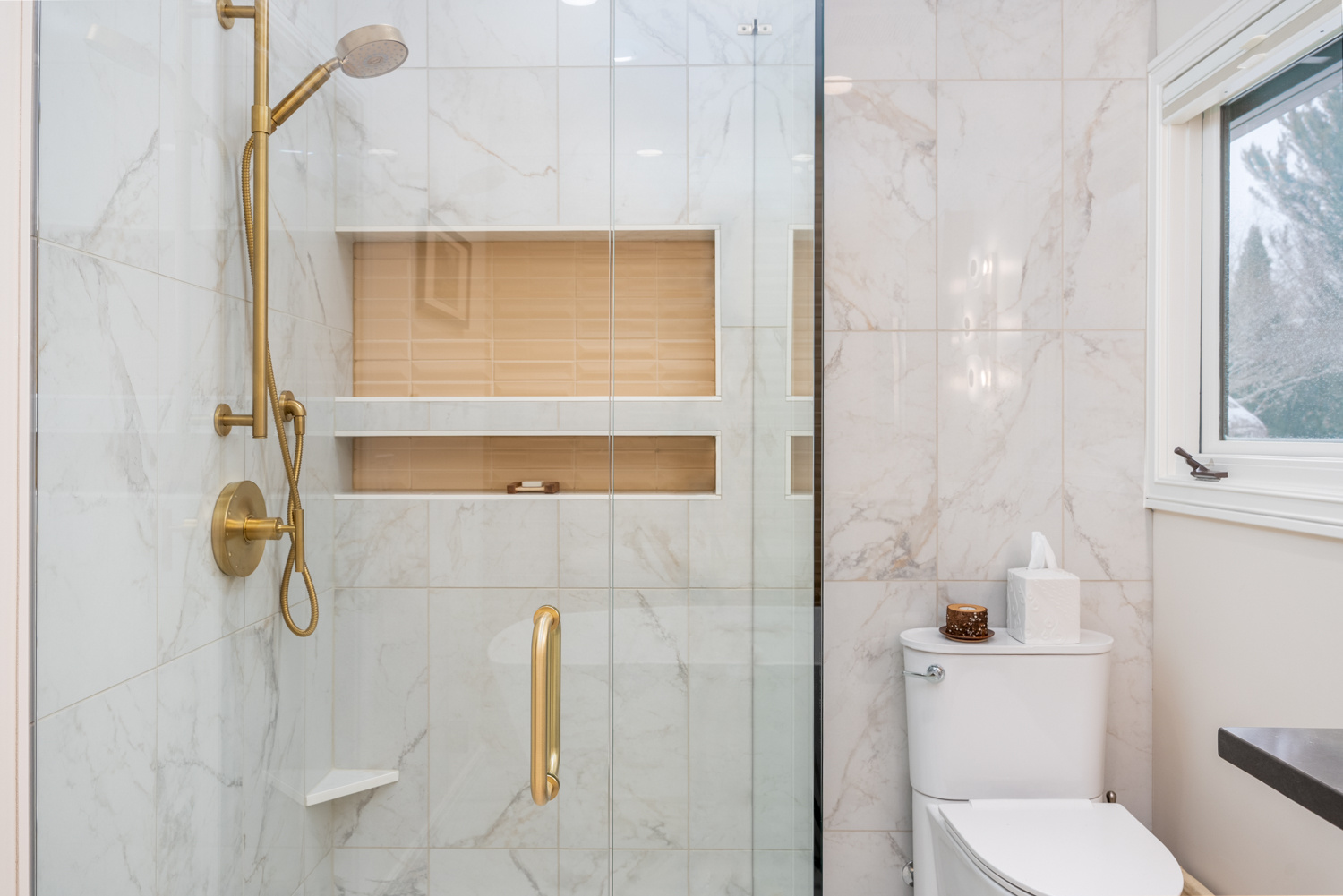 Full view of a luxurious walk-in shower with gold fixtures, built-in shelving, and marble tile walls, part of a whole home remodel in Portland, OR by Creekstone Design + Remodel