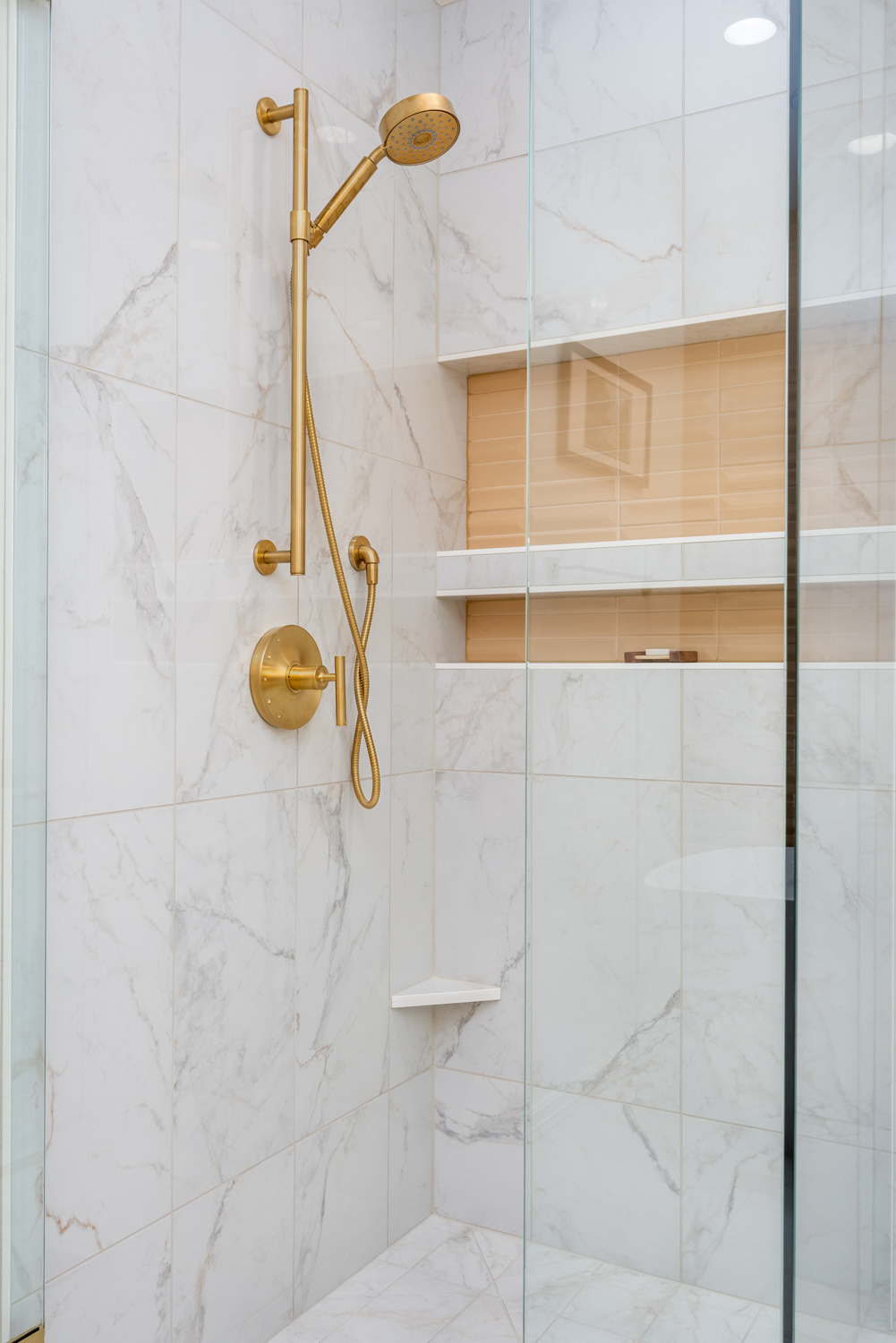 Luxury walk-in shower with marble tile walls, gold shower fixtures, and built-in shelving, part of a whole home remodel in Portland, OR by Creekstone Design + Remodel