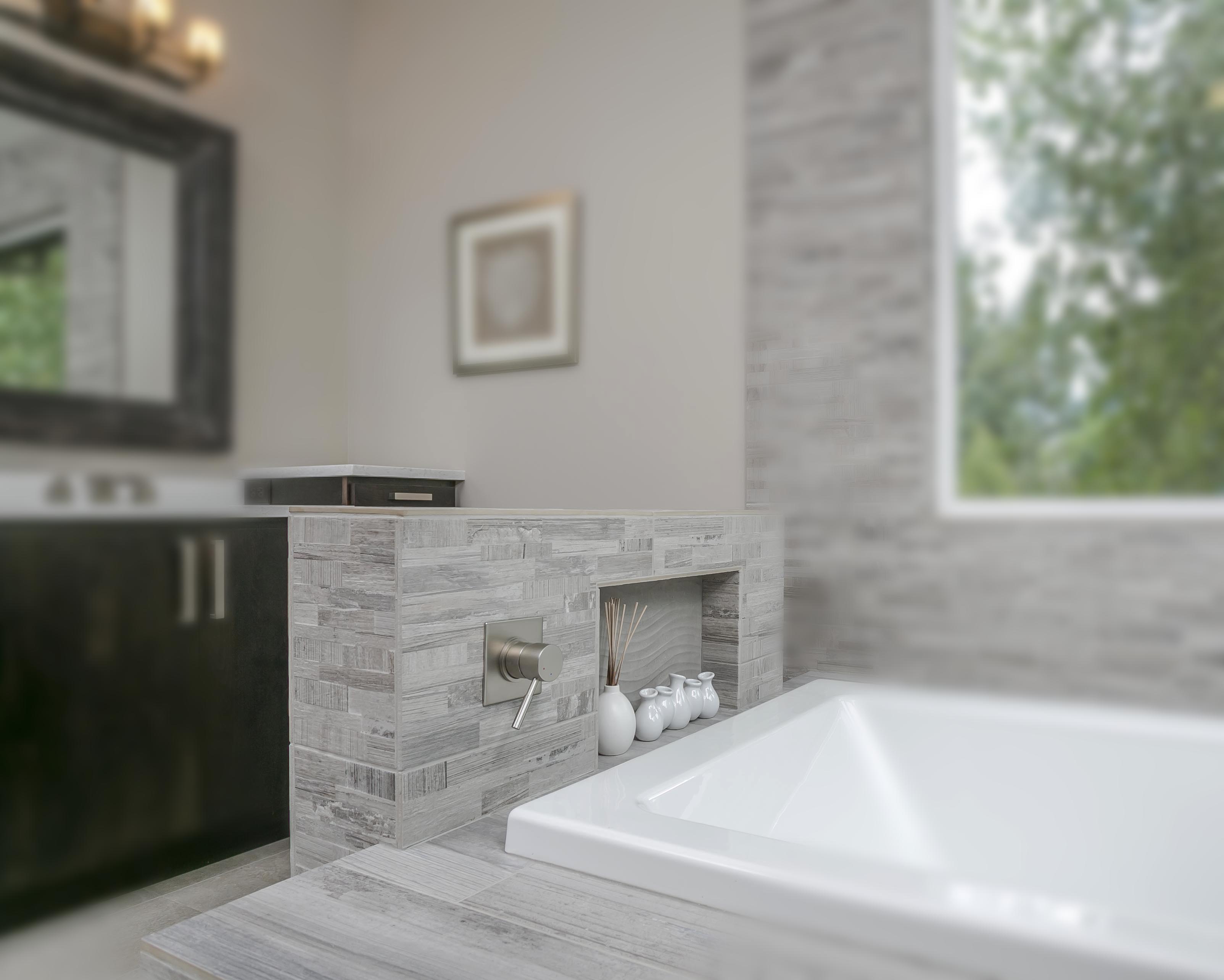 Built in bathtub with grey tiles next to a window